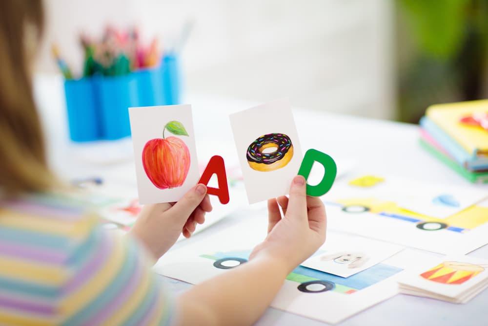 Child holding the letters A and D and phonics flashcards with a picture of an apple and a donut.