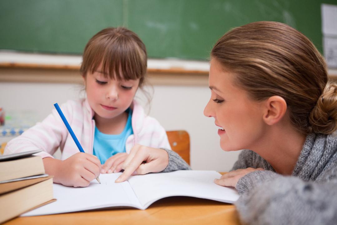 Girl writing in notebook with teacher.