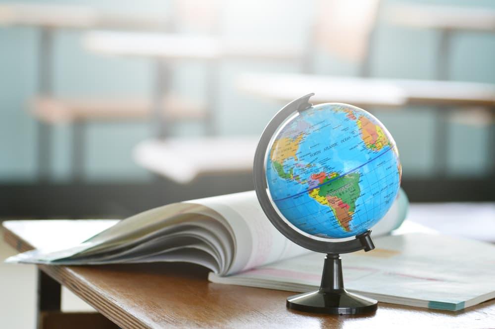 Small model globe sitting on desk next to a geography workbook.
