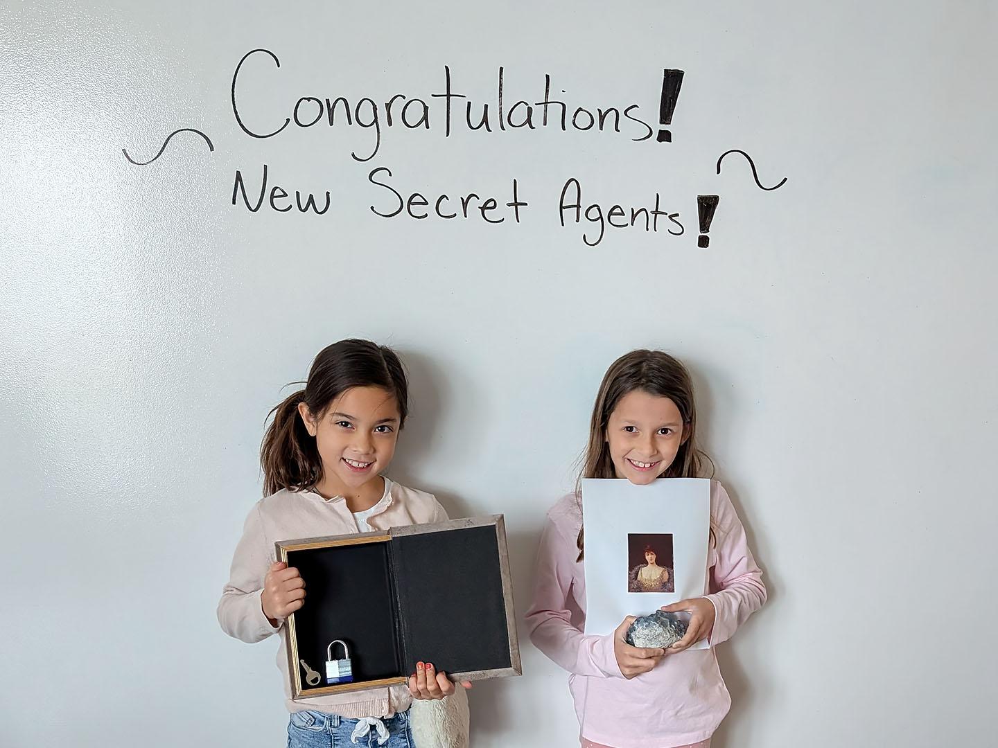 Two girls holding up props for the math escape room they completed.