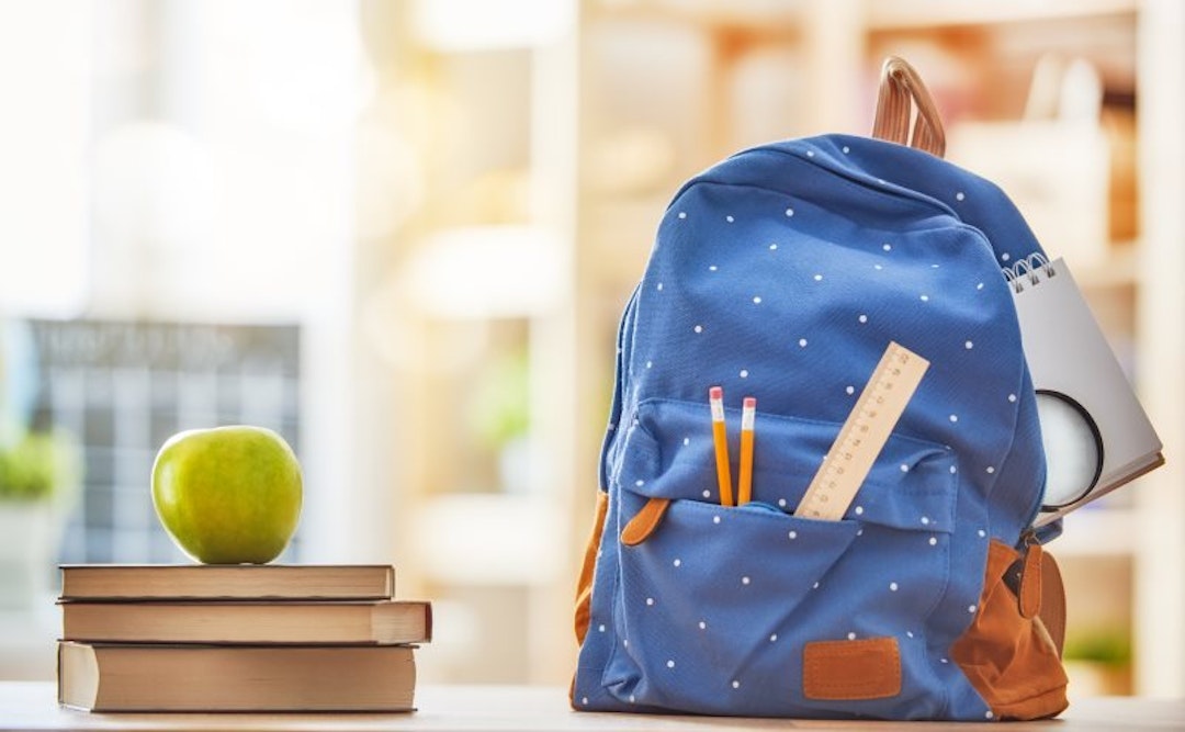 A blue backpack next to an apple stacked on top of three books