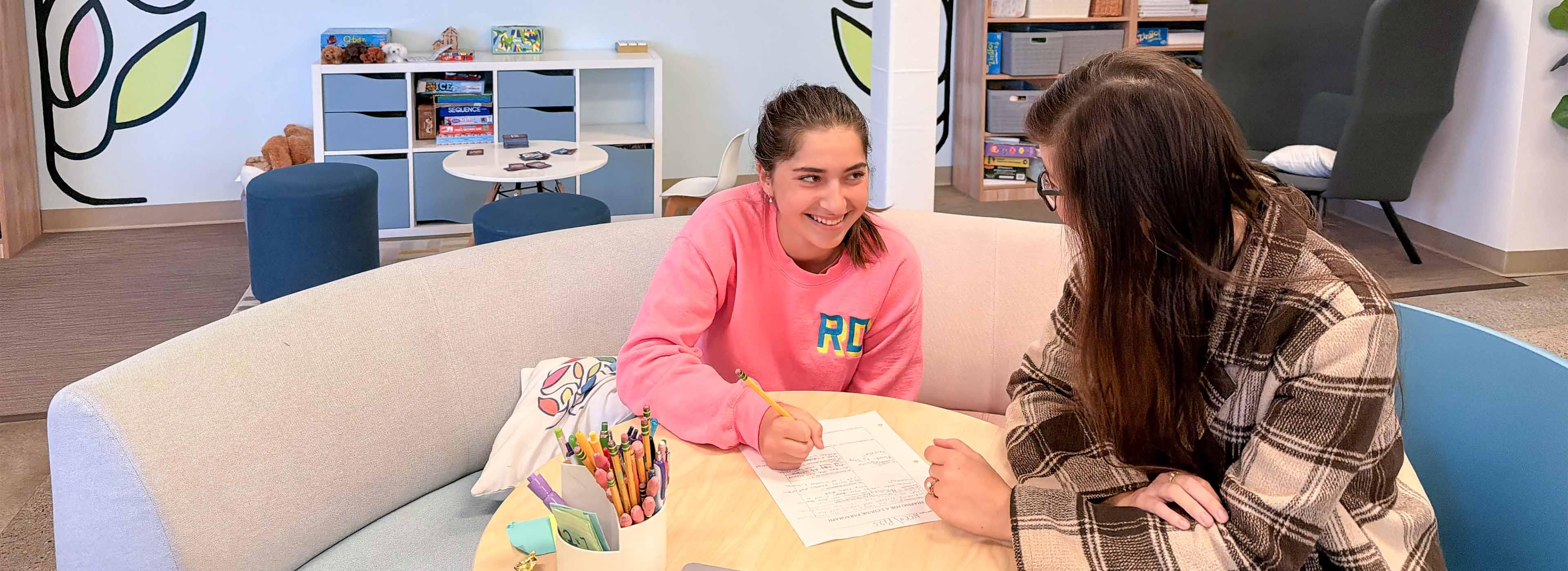Student smiling at teacher while working on assignment at a desk.