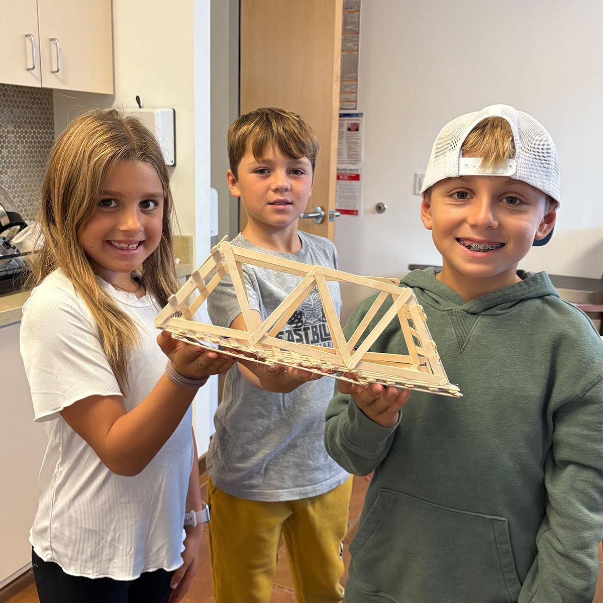 Group of 3 students holding a wooden bridge made out of popsicle sticks.