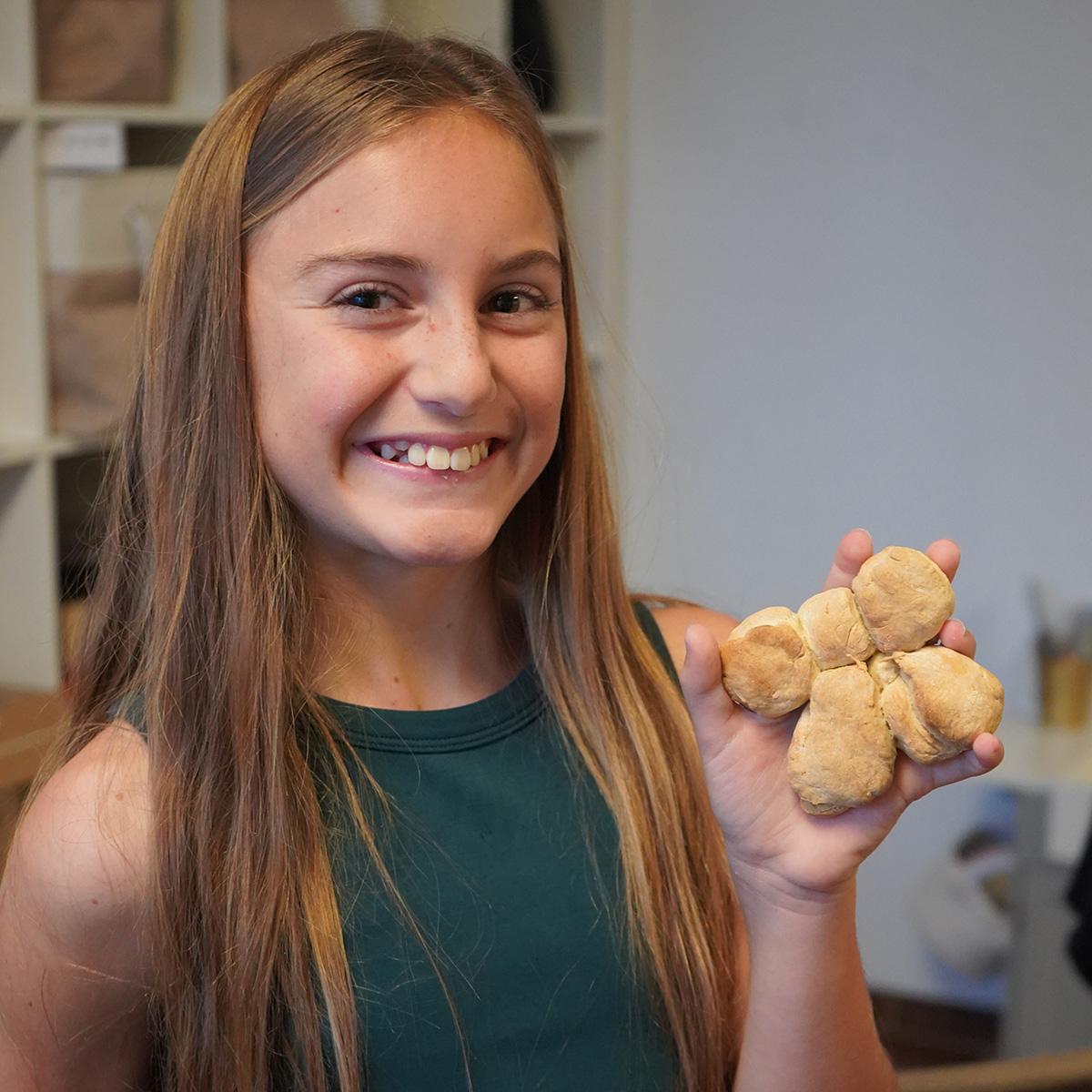 Girl smiling as she holds baked bread shaped as a bow.