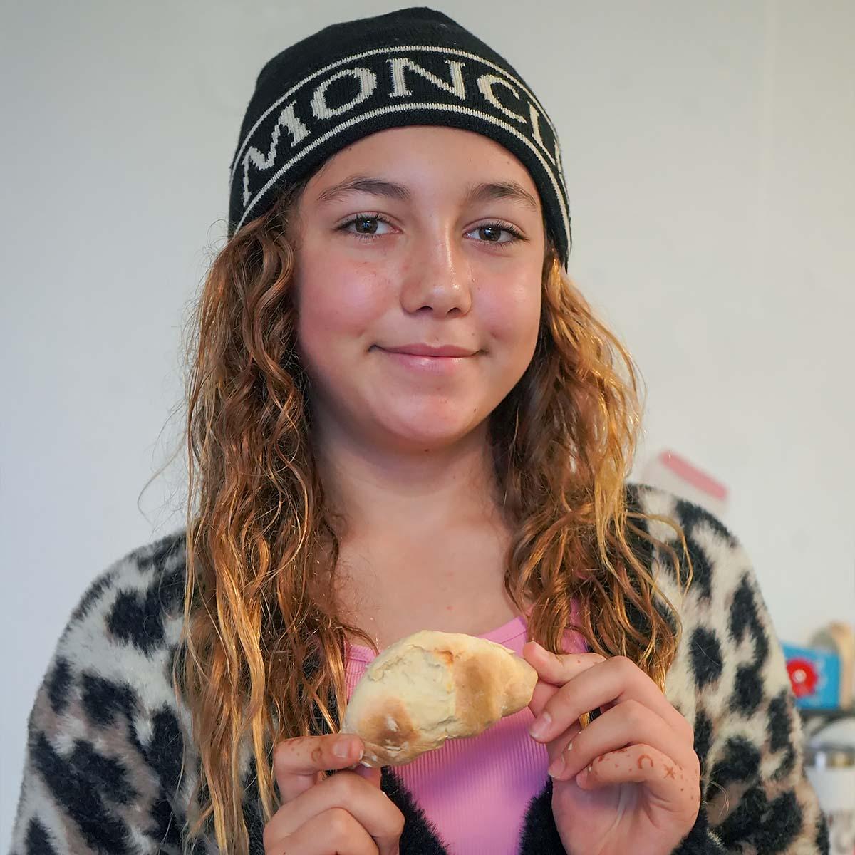 Girl holding piece of bread, smiling.