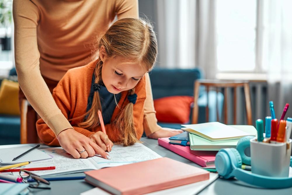 Young girl filling out her school notebook with her tutor.